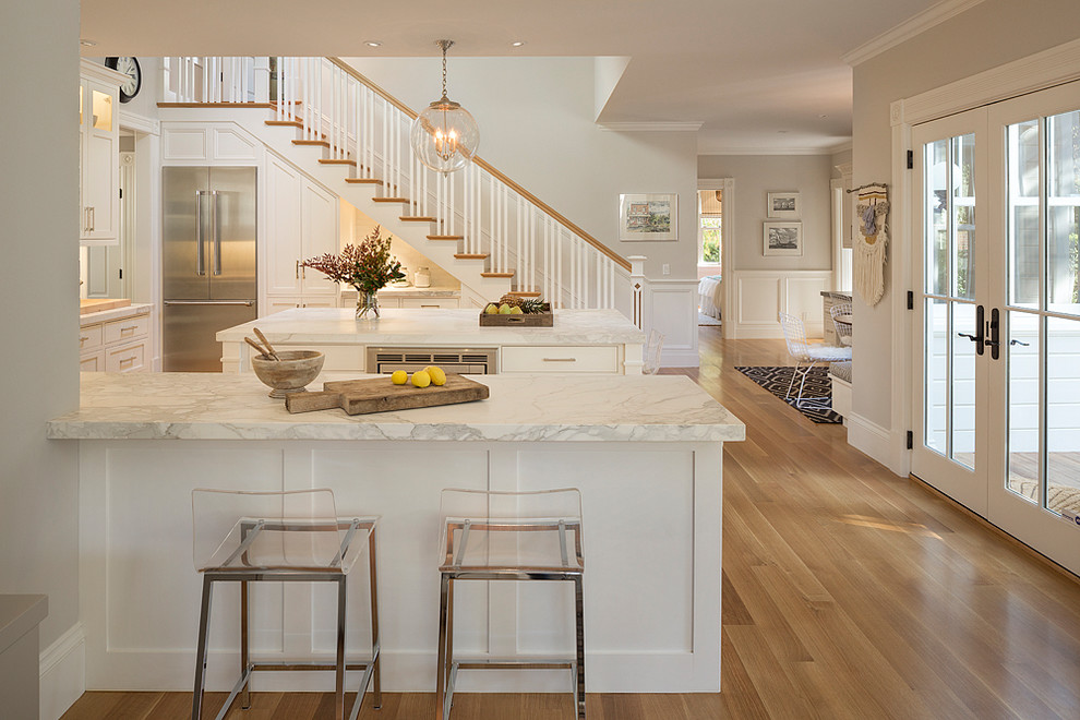 This is an example of a traditional u-shaped kitchen in San Francisco with shaker cabinets, white cabinets, white splashback, stainless steel appliances, medium hardwood floors, with island and brown floor.