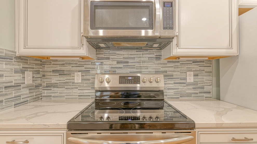 Kitchen - mid-sized medium tone wood floor kitchen idea in Charlotte with a single-bowl sink, shaker cabinets, white cabinets, quartzite countertops, gray backsplash, glass tile backsplash, stainless steel appliances and white countertops