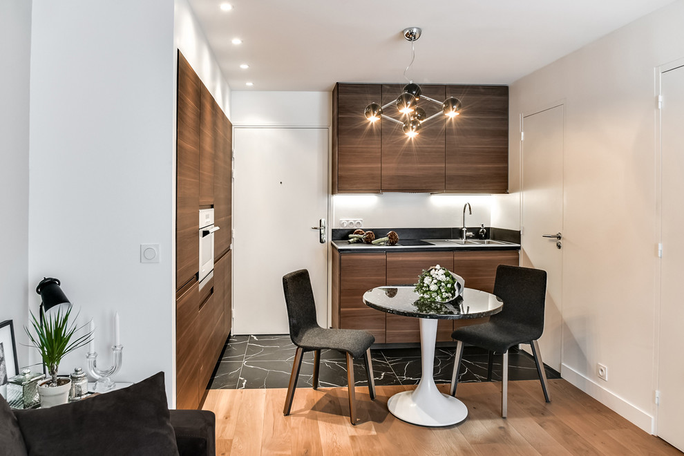 This is an example of a small contemporary single-wall eat-in kitchen in Paris with flat-panel cabinets, dark wood cabinets, stainless steel appliances, no island and black floor.