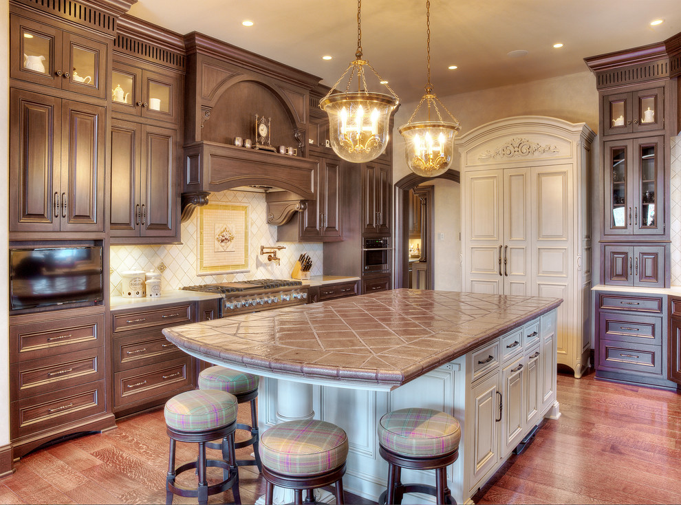This is an example of a large traditional l-shaped eat-in kitchen in Kansas City with raised-panel cabinets, brown cabinets, tile benchtops, white splashback, ceramic splashback, stainless steel appliances and with island.