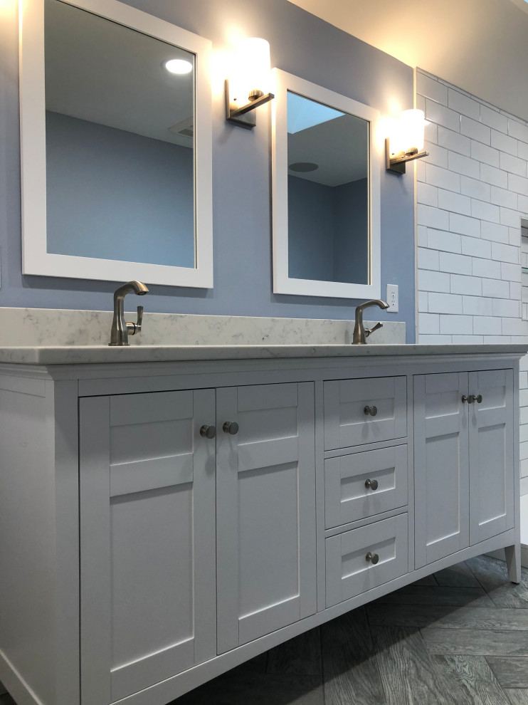 This is an example of a mid-sized arts and crafts master bathroom in Indianapolis with shaker cabinets, white cabinets, a freestanding tub, a corner shower, a two-piece toilet, white tile, subway tile, blue walls, porcelain floors, an undermount sink, quartzite benchtops, grey floor, a hinged shower door, white benchtops, a niche, a double vanity, a freestanding vanity, vaulted and planked wall panelling.