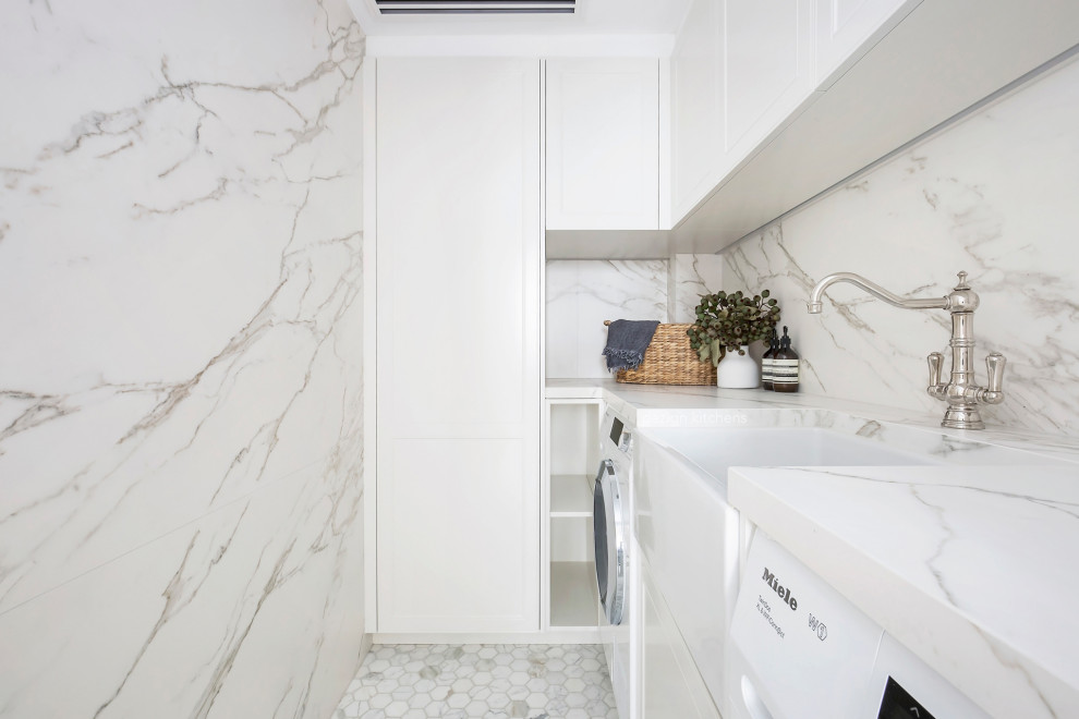 Inspiration for a mid-sized transitional l-shaped dedicated laundry room in Sydney with a farmhouse sink, recessed-panel cabinets, white cabinets, marble benchtops, multi-coloured splashback, marble splashback, white walls, medium hardwood floors, an integrated washer and dryer, white floor and multi-coloured benchtop.
