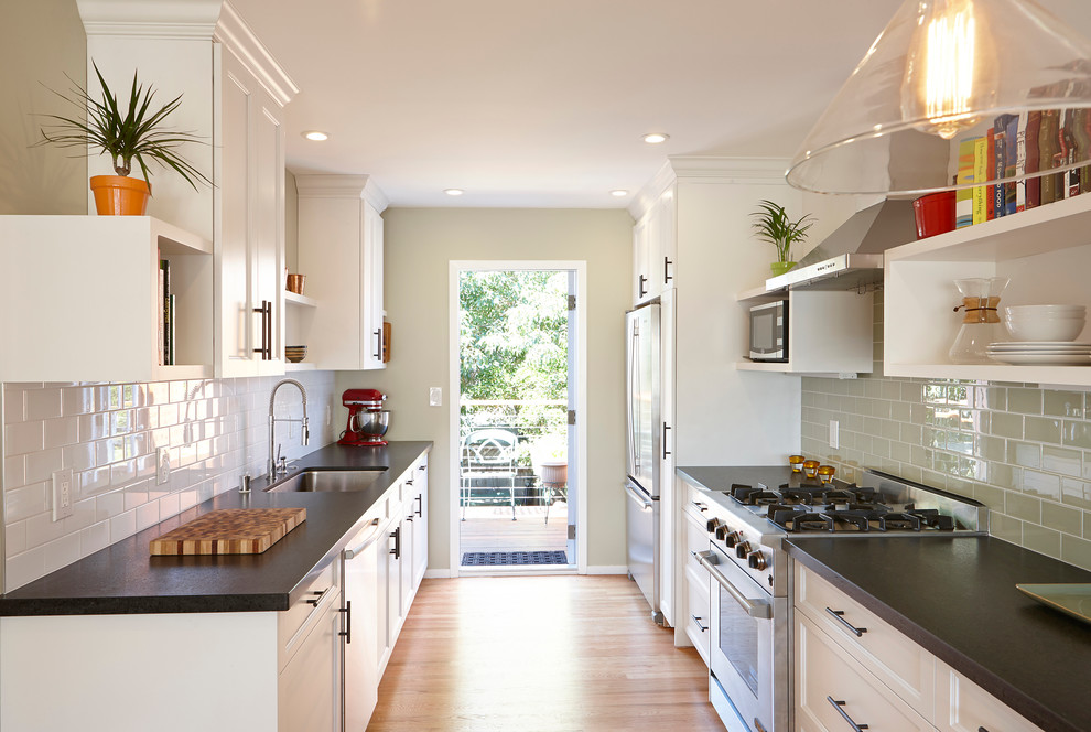 Photo of a transitional galley separate kitchen in San Francisco with an undermount sink, recessed-panel cabinets, white cabinets, subway tile splashback, stainless steel appliances and grey splashback.