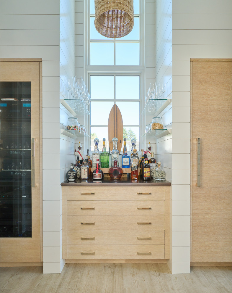 Beach style kitchen in New York with an integrated sink, flat-panel cabinets, light wood cabinets, stainless steel benchtops, panelled appliances, light hardwood floors, with island, beige floor and vaulted.