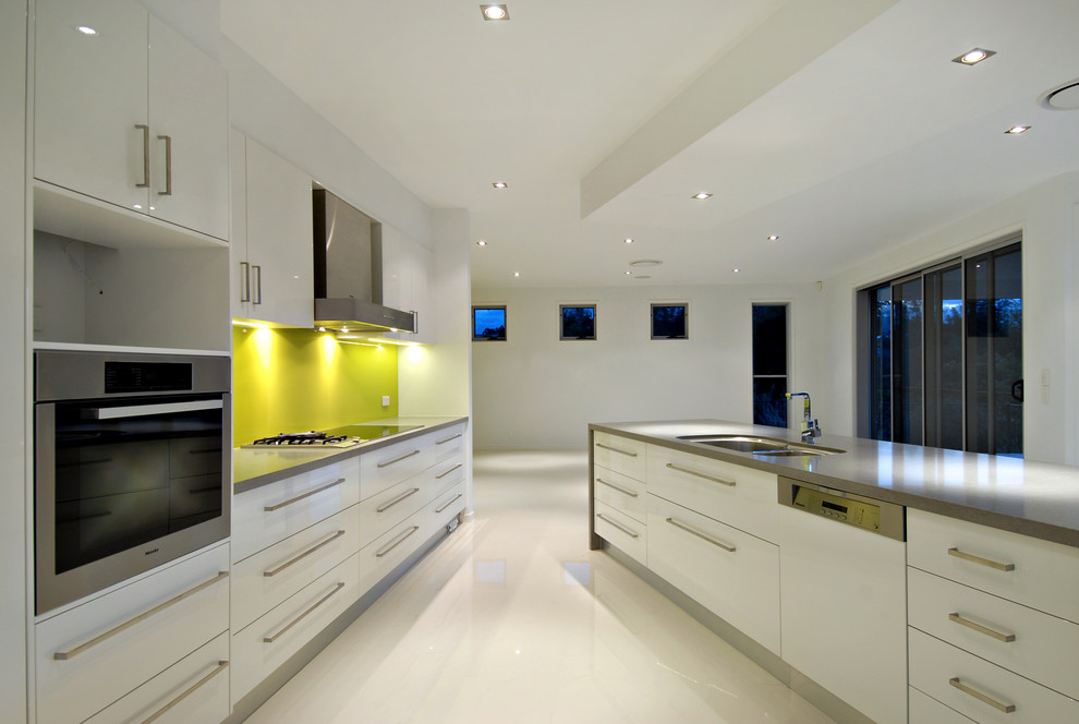 This is an example of a large modern galley kitchen pantry in Brisbane with a double-bowl sink, yellow splashback, porcelain splashback, stainless steel appliances, porcelain floors and no island.