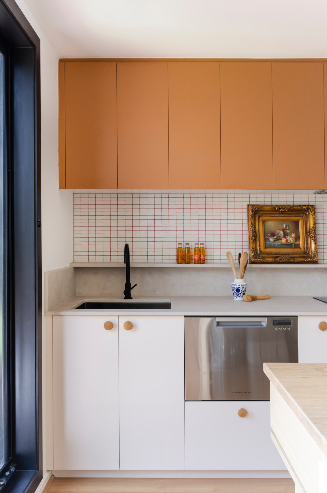 Bild på ett mellanstort eklektiskt gul gult kök, med en undermonterad diskho, släta luckor, orange skåp, träbänkskiva, vitt stänkskydd, stänkskydd i mosaik, rostfria vitvaror, laminatgolv, en köksö och gult golv