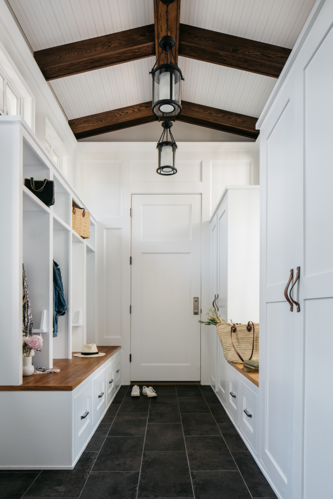 This is an example of a large country mudroom in Chicago with white walls, porcelain floors, a single front door, a white front door, black floor and exposed beam.