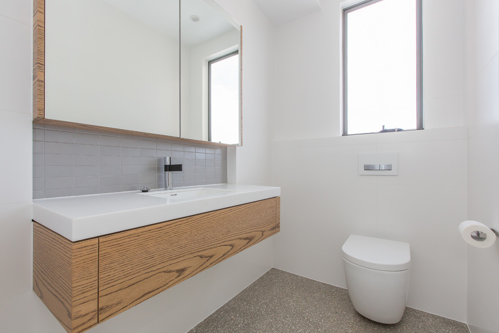 This is an example of a small contemporary kids bathroom in Gold Coast - Tweed with flat-panel cabinets, medium wood cabinets, a drop-in tub, an open shower, a two-piece toilet, gray tile, porcelain tile, white walls, concrete floors, an undermount sink and solid surface benchtops.