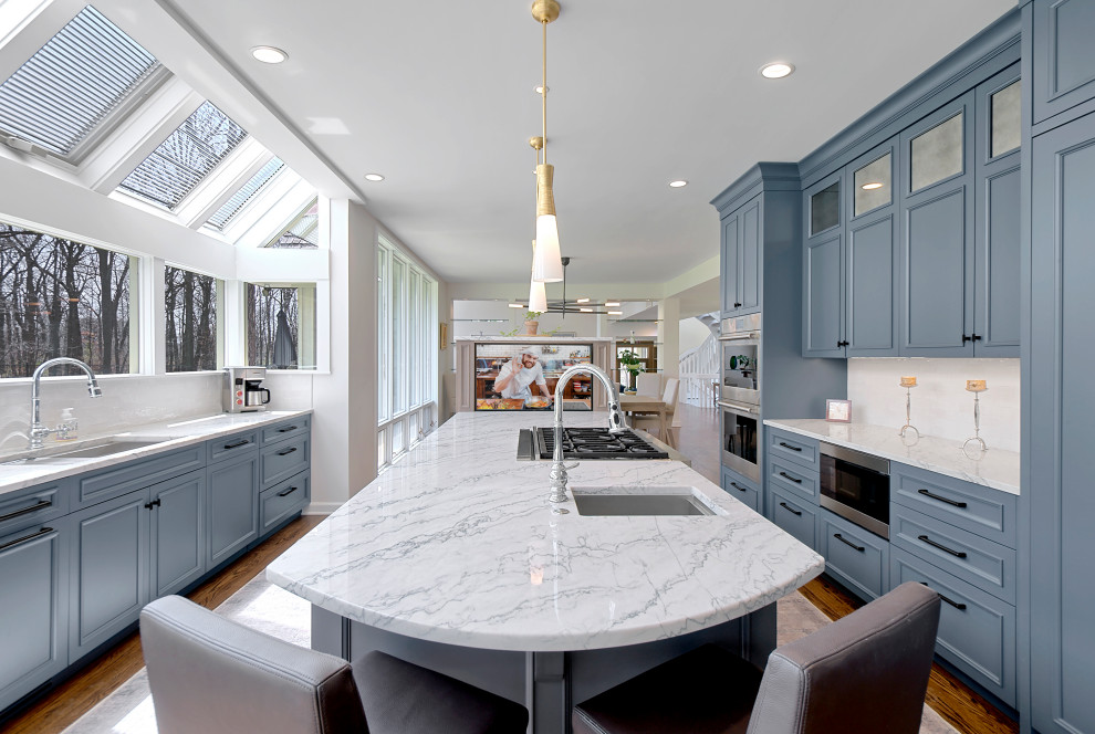 Design ideas for a large transitional u-shaped eat-in kitchen in Chicago with an undermount sink, recessed-panel cabinets, blue cabinets, quartz benchtops, white splashback, stone slab splashback, stainless steel appliances, medium hardwood floors, with island, brown floor and white benchtop.