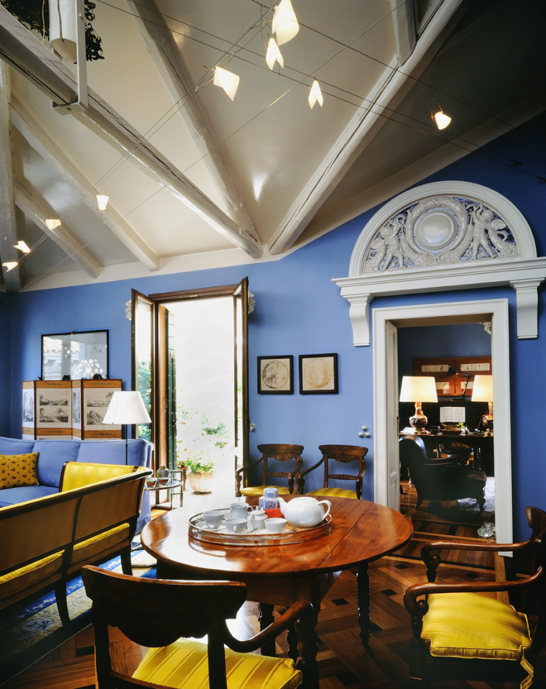 Immagine di una sala da pranzo aperta verso il soggiorno eclettica di medie dimensioni con pareti blu, parquet chiaro, camino classico, cornice del camino in pietra e travi a vista