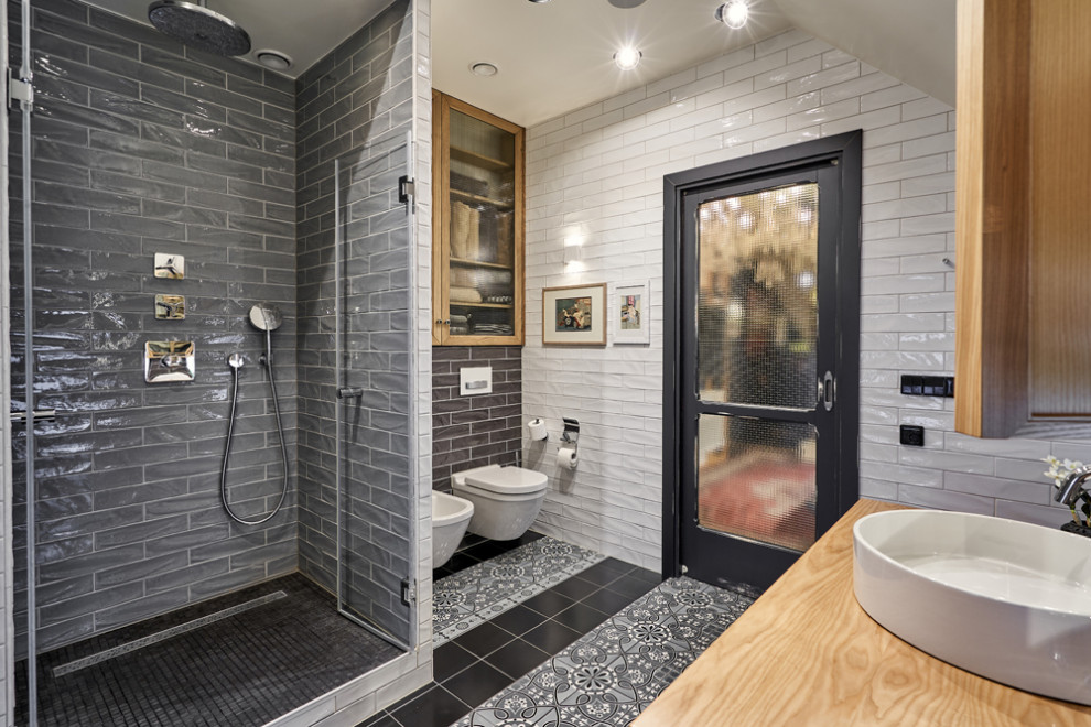 Inredning av ett stort brun brunt badrum med dusch, med luckor med infälld panel, orange skåp, ett fristående badkar, en kantlös dusch, en vägghängd toalettstol, grå kakel, tunnelbanekakel, grå väggar, klinkergolv i keramik, ett fristående handfat, träbänkskiva, grått golv och dusch med gångjärnsdörr