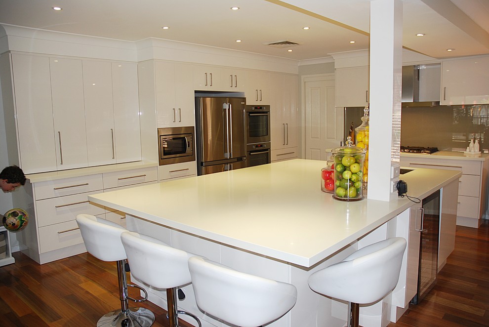 Photo of a large modern l-shaped eat-in kitchen in Sydney with an undermount sink, flat-panel cabinets, white cabinets, solid surface benchtops, brown splashback, glass sheet splashback, stainless steel appliances, medium hardwood floors and with island.