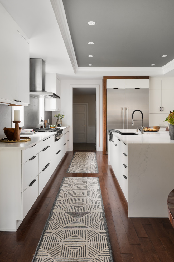 Large transitional u-shaped eat-in kitchen in Montreal with an undermount sink, flat-panel cabinets, white cabinets, quartz benchtops, grey splashback, slate splashback, stainless steel appliances, dark hardwood floors, with island, brown floor, white benchtop and coffered.