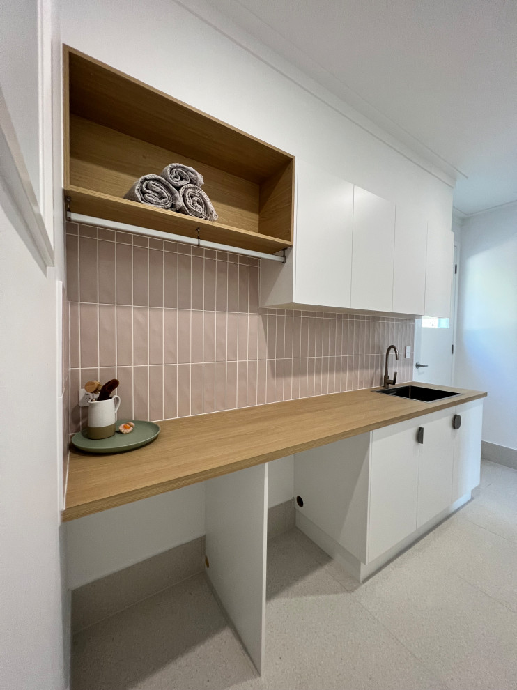 Contemporary galley dedicated laundry room in Sunshine Coast with a drop-in sink, flat-panel cabinets, white cabinets, laminate benchtops, pink splashback, subway tile splashback, white walls, ceramic floors, a side-by-side washer and dryer, grey floor and brown benchtop.
