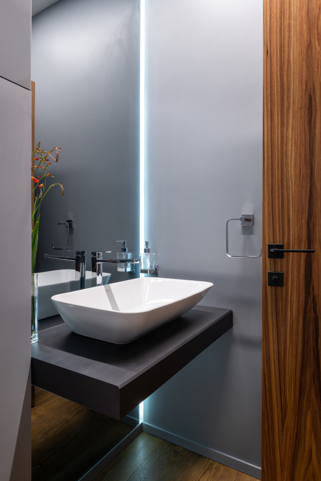 Inspiration for a small contemporary powder room in Yekaterinburg with a wall-mount toilet, grey walls, porcelain floors, a drop-in sink, wood benchtops, brown floor, black benchtops, a floating vanity and wallpaper.