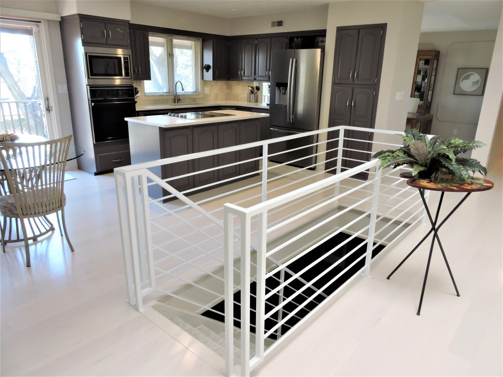 Example of a mid-sized transitional l-shaped light wood floor and white floor open concept kitchen design with a double-bowl sink, raised-panel cabinets, dark wood cabinets, quartz countertops, white backsplash, ceramic backsplash, stainless steel appliances, an island and white countertops