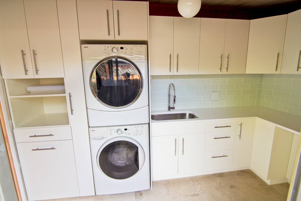 Photo of a small midcentury l-shaped utility room in San Francisco with an undermount sink, flat-panel cabinets, white cabinets, quartz benchtops, white walls, travertine floors and a stacked washer and dryer.