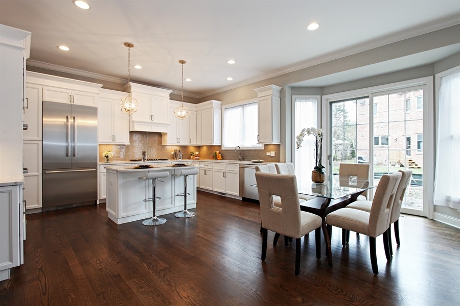 Inspiration for a large transitional l-shaped dark wood floor eat-in kitchen remodel in Chicago with an undermount sink, shaker cabinets, white cabinets, quartz countertops, beige backsplash, subway tile backsplash, stainless steel appliances and an island