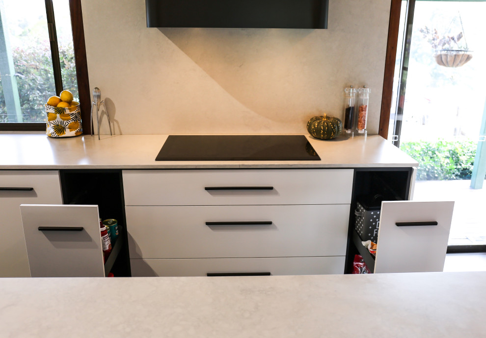 This is an example of a large contemporary l-shaped eat-in kitchen in Other with a double-bowl sink, flat-panel cabinets, white cabinets, quartz benchtops, multi-coloured splashback, engineered quartz splashback, black appliances, laminate floors, with island, brown floor, multi-coloured benchtop and exposed beam.