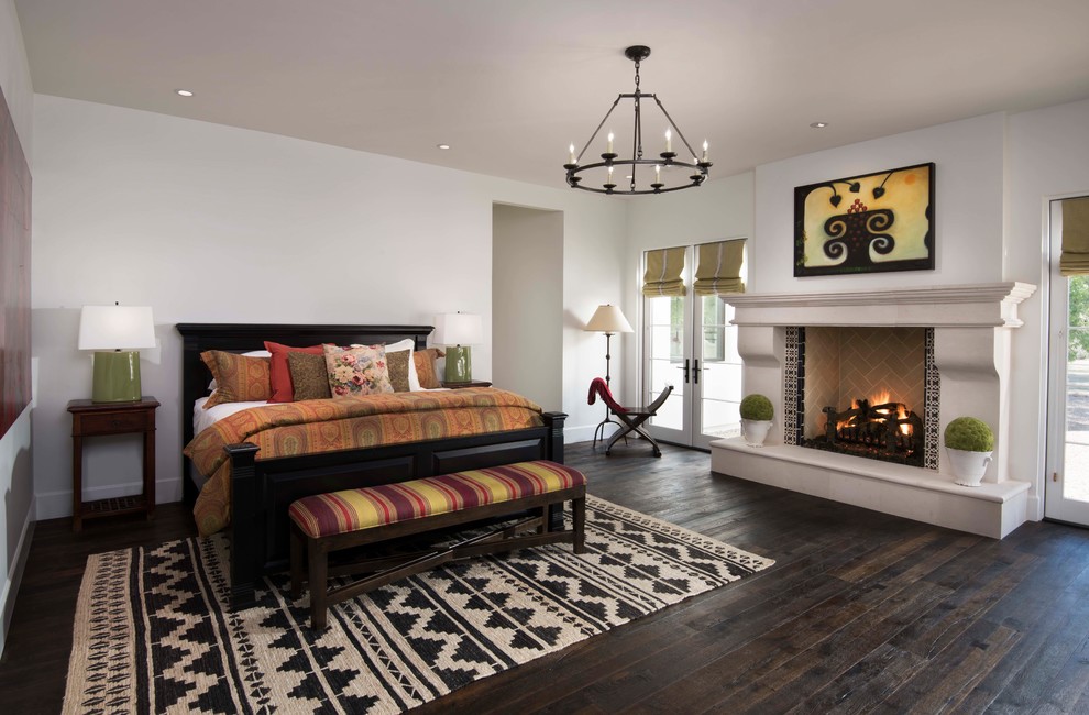 Mediterranean master bedroom in Phoenix with white walls, dark hardwood floors, a standard fireplace, a tile fireplace surround and brown floor.