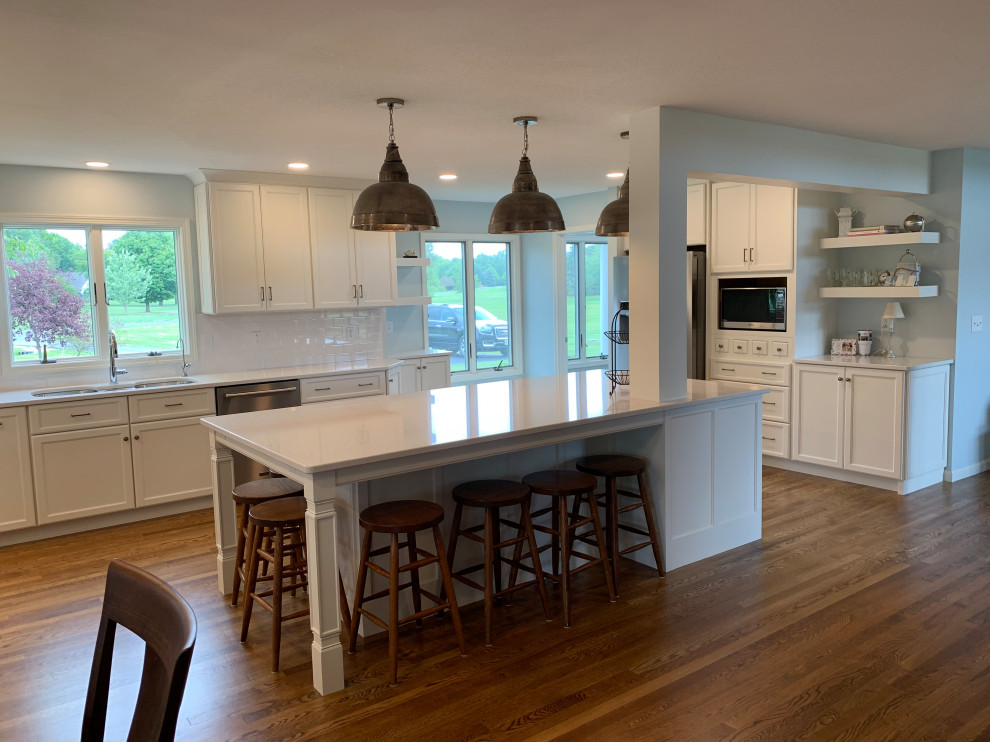 Large transitional u-shaped medium tone wood floor and brown floor open concept kitchen photo with an undermount sink, recessed-panel cabinets, white cabinets, quartz countertops, white backsplash, stainless steel appliances, an island and white countertops
