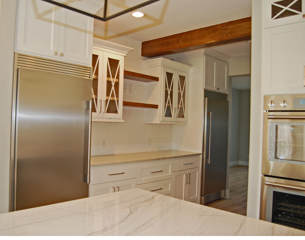 This is an example of a large country u-shaped eat-in kitchen in Houston with a farmhouse sink, shaker cabinets, white cabinets, quartzite benchtops, white splashback, ceramic splashback, stainless steel appliances, light hardwood floors, with island, beige floor and white benchtop.