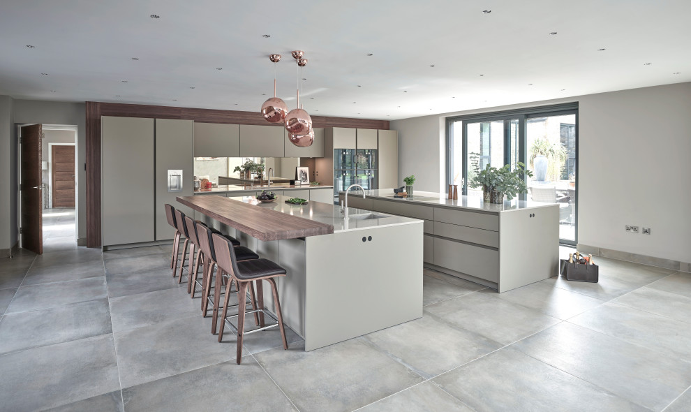 Photo of an expansive contemporary open plan kitchen in Other with flat-panel cabinets, beige cabinets, quartzite benchtops, brown splashback, mirror splashback, stainless steel appliances, porcelain floors, multiple islands, grey floor and beige benchtop.