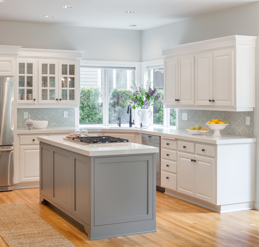 Inspiration for a mid-sized transitional u-shaped open plan kitchen in Portland with an undermount sink, raised-panel cabinets, white cabinets, quartzite benchtops, grey splashback, ceramic splashback, stainless steel appliances, light hardwood floors, with island and beige floor.