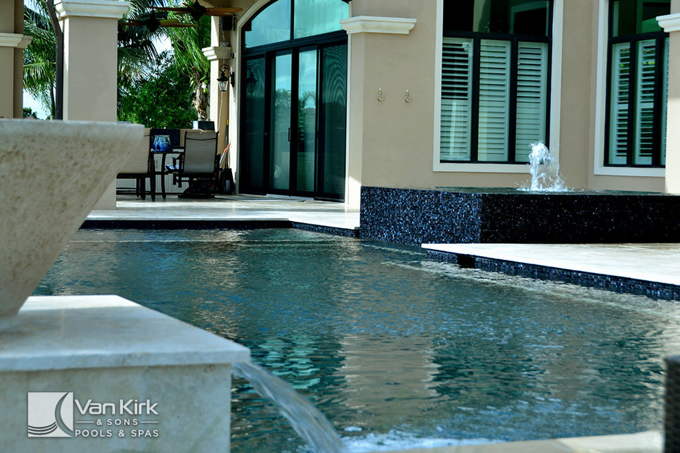 Photo of a large contemporary backyard rectangular pool in Miami with a hot tub and natural stone pavers.