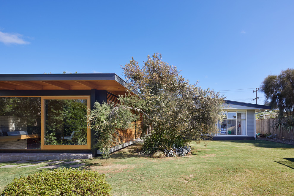 This is an example of a small midcentury one-storey brown house exterior in Melbourne with wood siding, a flat roof and a metal roof.