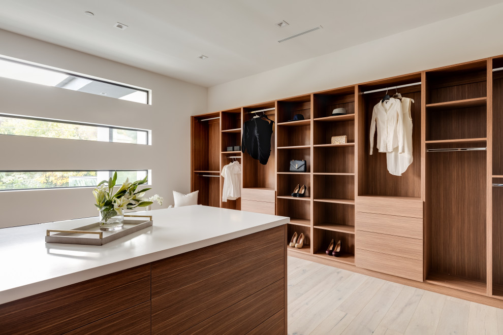 Expansive contemporary gender-neutral walk-in wardrobe in Los Angeles with flat-panel cabinets, medium wood cabinets, light hardwood floors and brown floor.