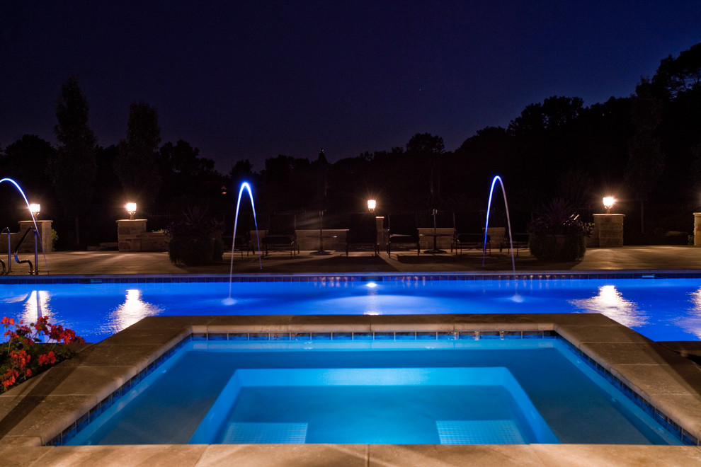 This is an example of a large traditional backyard rectangular lap pool in Chicago with a hot tub and natural stone pavers.