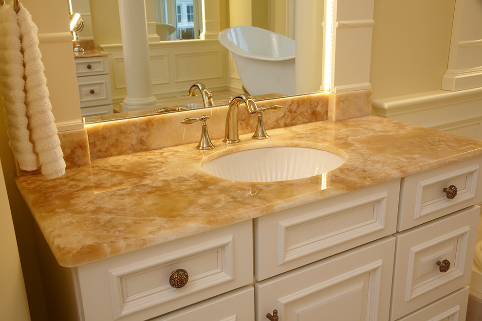 Photo of a mid-sized traditional master bathroom in Boston with raised-panel cabinets, beige cabinets, a claw-foot tub, a corner shower, a one-piece toilet, beige tile, marble, yellow walls, marble floors, an undermount sink, onyx benchtops, beige floor and an open shower.