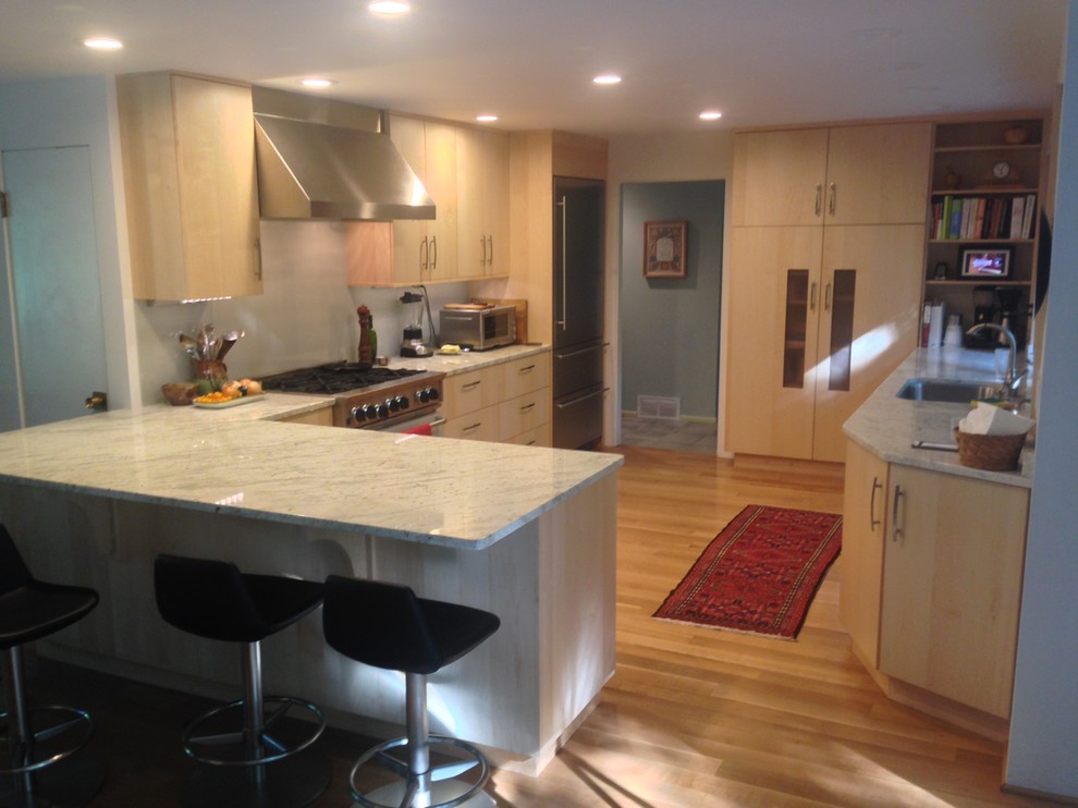 Photo of a contemporary u-shaped eat-in kitchen in New York with an undermount sink, flat-panel cabinets, light wood cabinets, granite benchtops, grey splashback, glass sheet splashback and coloured appliances.