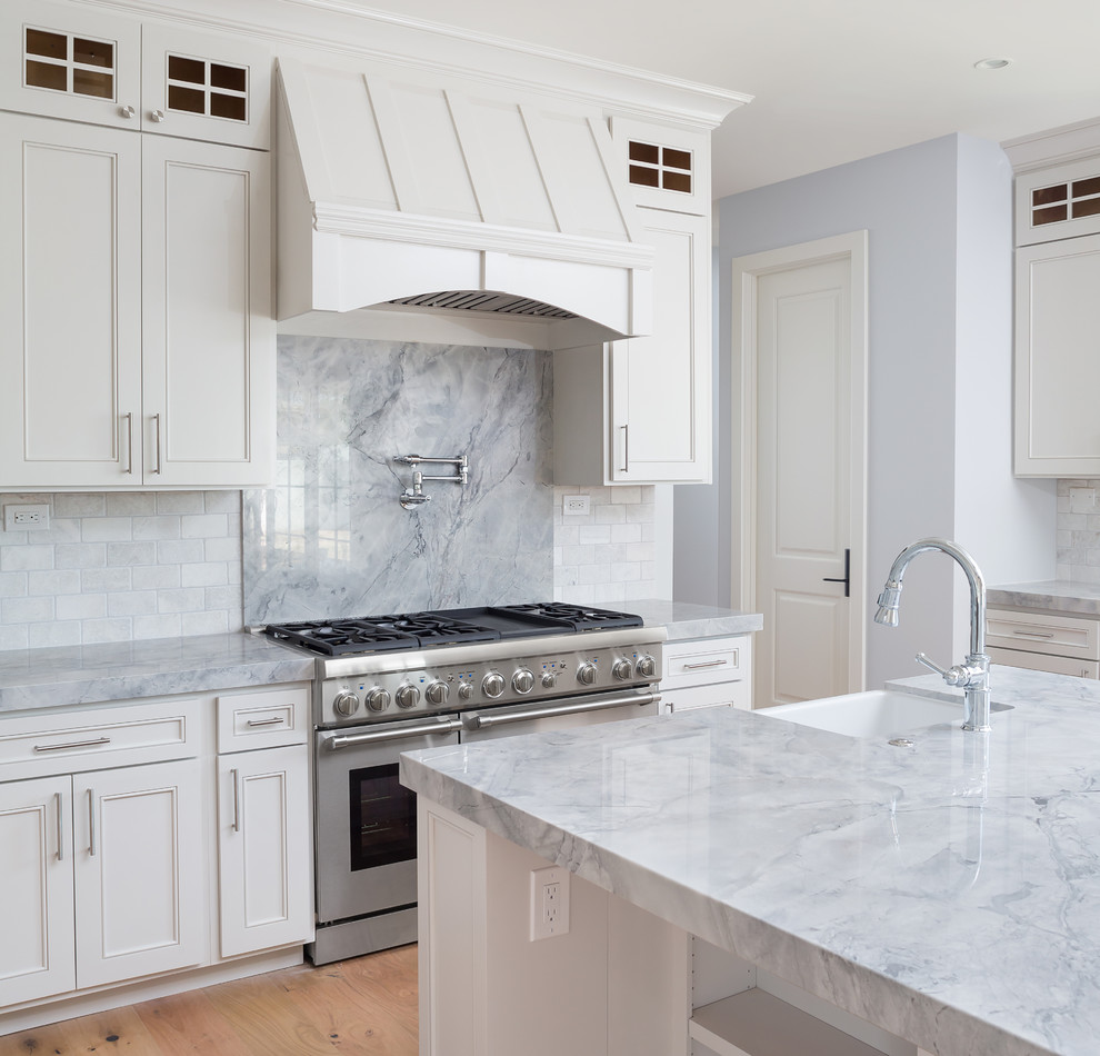 Example of a large transitional u-shaped light wood floor open concept kitchen design in Phoenix with a farmhouse sink, shaker cabinets, white cabinets, quartzite countertops, gray backsplash, stone tile backsplash, stainless steel appliances and an island