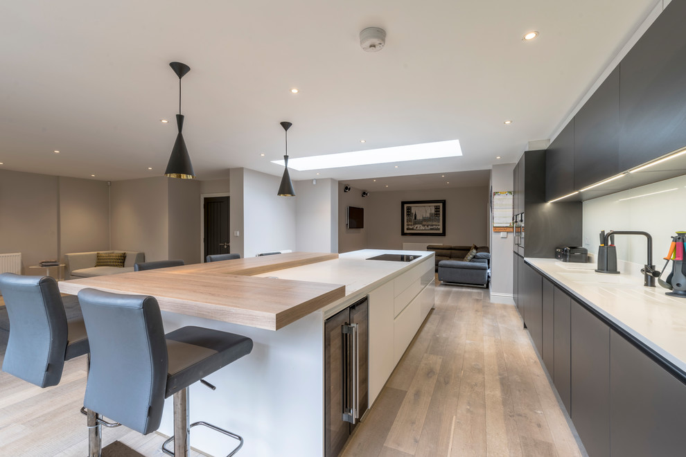 Design ideas for a large contemporary l-shaped open plan kitchen in Cheshire with a drop-in sink, flat-panel cabinets, solid surface benchtops, white splashback, glass sheet splashback, black appliances, light hardwood floors and with island.