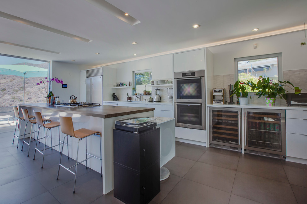 This is an example of a contemporary galley kitchen in Los Angeles with flat-panel cabinets, white cabinets, stainless steel appliances and with island.