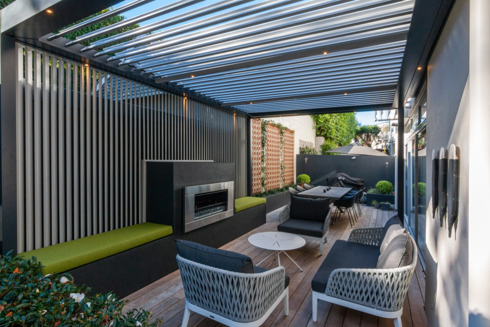 Small contemporary courtyard patio in Auckland with with fireplace, decking and a pergola.