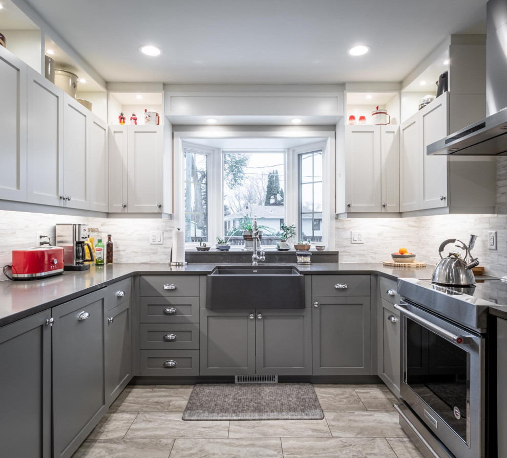 Example of a mid-sized transitional u-shaped gray floor kitchen design with a farmhouse sink, shaker cabinets, gray cabinets, white backsplash, stainless steel appliances, no island and gray countertops