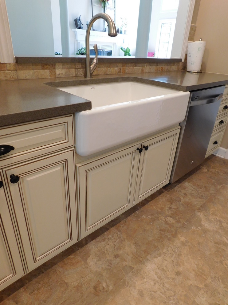 Example of a mid-sized transitional galley vinyl floor enclosed kitchen design with a farmhouse sink, raised-panel cabinets, beige cabinets, solid surface countertops, multicolored backsplash, stone tile backsplash, stainless steel appliances and no island