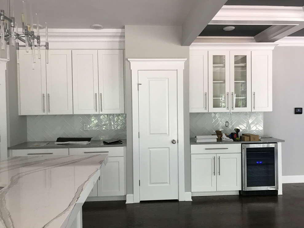 Photo of a large traditional galley open plan kitchen in New York with a double-bowl sink, recessed-panel cabinets, white cabinets, granite benchtops, white splashback, ceramic splashback, stainless steel appliances, vinyl floors, with island, black floor and multi-coloured benchtop.