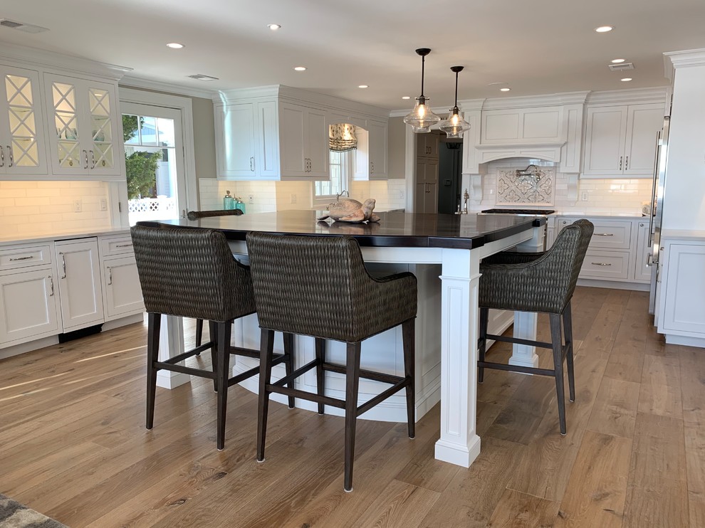 Eat-in kitchen - large transitional light wood floor and brown floor eat-in kitchen idea with recessed-panel cabinets, white cabinets, white backsplash, porcelain backsplash, stainless steel appliances, an island and white countertops