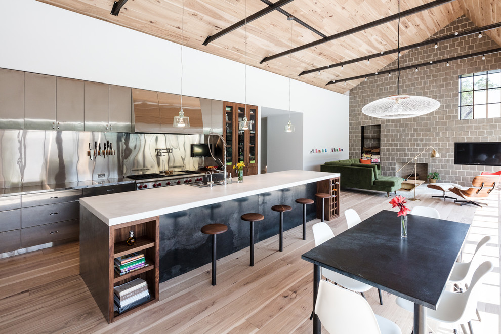 Design ideas for a large industrial galley open plan kitchen in Austin with a farmhouse sink, flat-panel cabinets, stainless steel cabinets, metallic splashback, light hardwood floors, with island, beige floor, stainless steel appliances, metal splashback and marble benchtops.