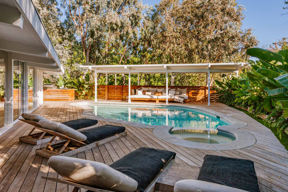 This is an example of a large midcentury backyard custom-shaped pool in Los Angeles with a hot tub and decking.