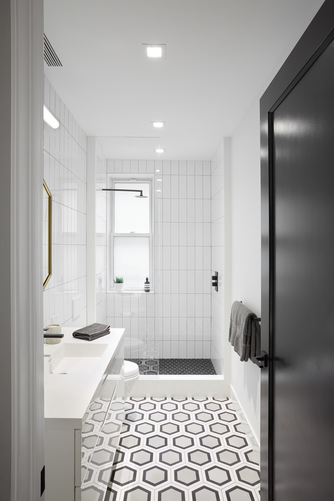 This is an example of a mid-sized modern 3/4 bathroom in New York with flat-panel cabinets, white cabinets, an open shower, a wall-mount toilet, white tile, subway tile, white walls, cement tiles, a wall-mount sink, solid surface benchtops, black floor and an open shower.