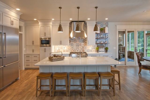 L-shaped kitchen photo with a farmhouse sink, flat-panel cabinets, white cabinets, quartz countertops, multicolored backsplash, ceramic backsplash, stainless steel appliances and an island