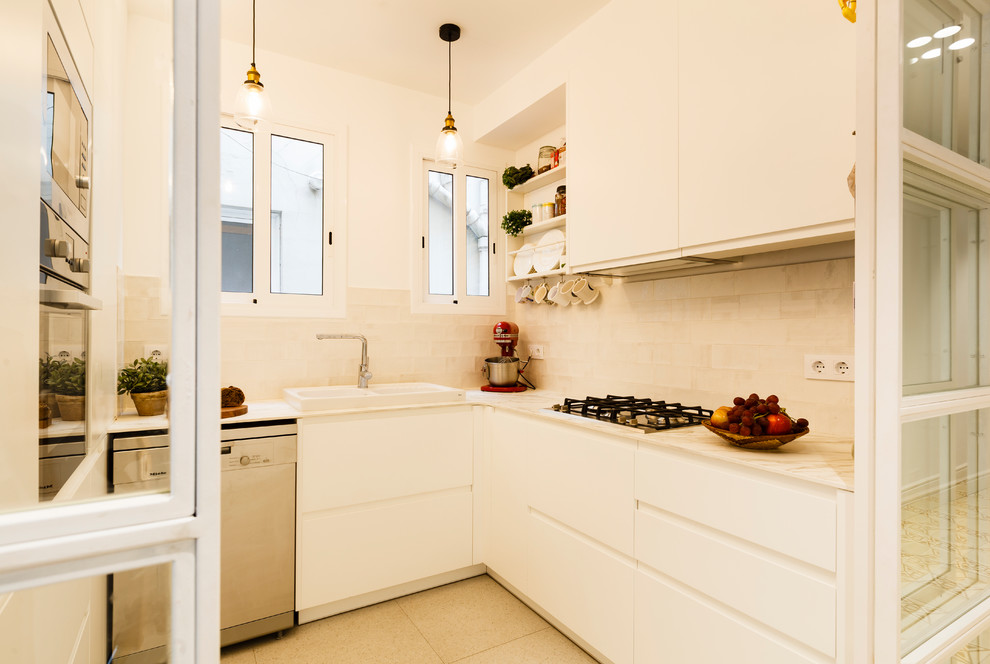 This is an example of a small scandinavian u-shaped separate kitchen in Barcelona with a double-bowl sink, flat-panel cabinets, white cabinets, stainless steel appliances, no island, beige floor and white benchtop.