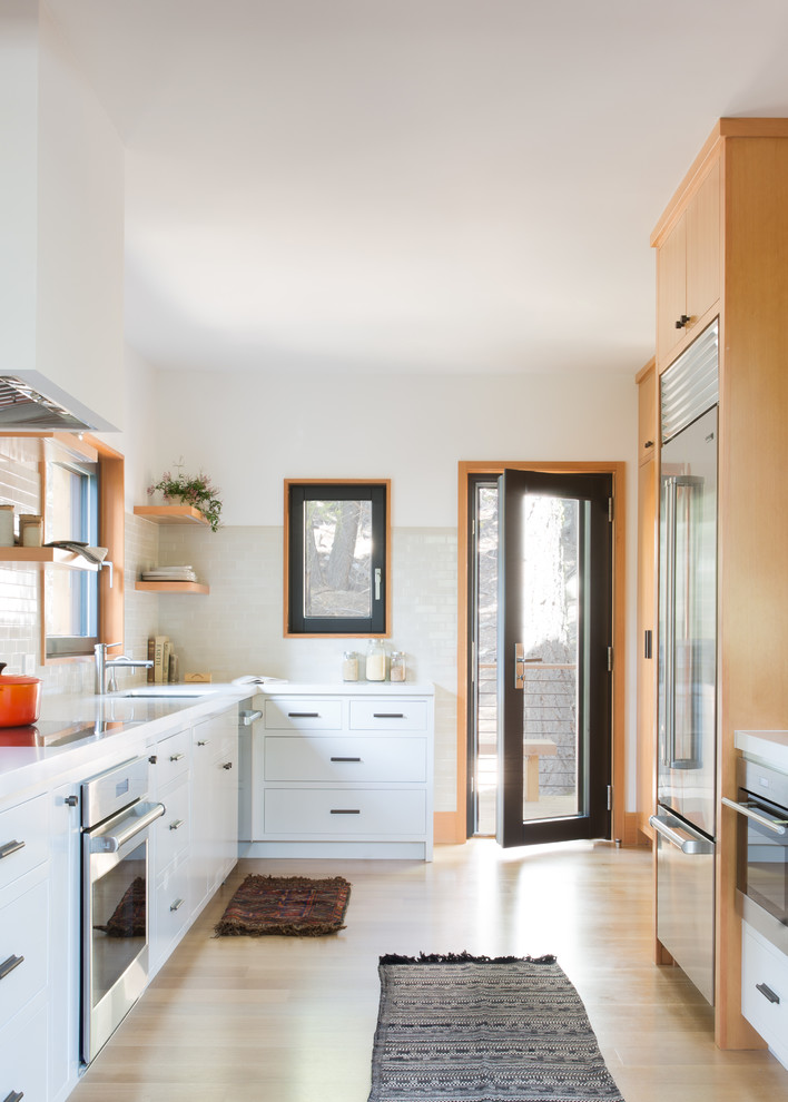 Photo of a country l-shaped kitchen in San Francisco with flat-panel cabinets, white cabinets, no island, white benchtop, an undermount sink, beige splashback, stainless steel appliances and light hardwood floors.