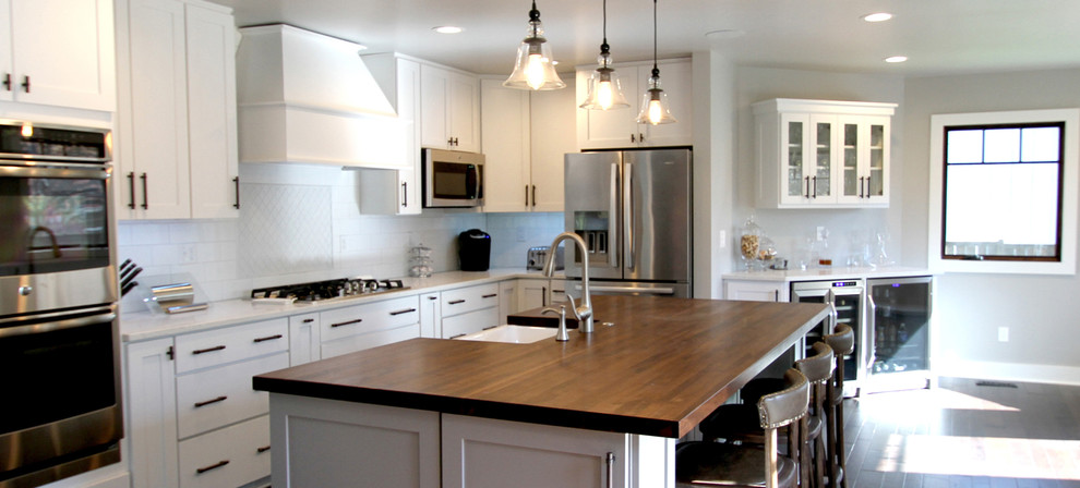 This is an example of a large contemporary single-wall eat-in kitchen in Kansas City with a farmhouse sink, raised-panel cabinets, white cabinets, wood benchtops, white splashback, ceramic splashback, stainless steel appliances, light hardwood floors, with island, grey floor and white benchtop.