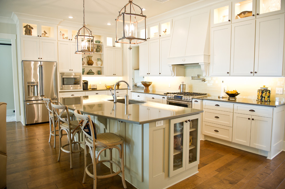 Inspiration for a traditional l-shaped kitchen in New Orleans with an undermount sink, shaker cabinets, white cabinets, white splashback, glass sheet splashback, stainless steel appliances, dark hardwood floors and with island.